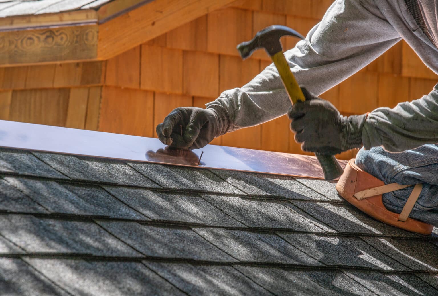 A contractor with hammer and nails demonstrates an answer to the question. Can you install a metal roof over shingles?
