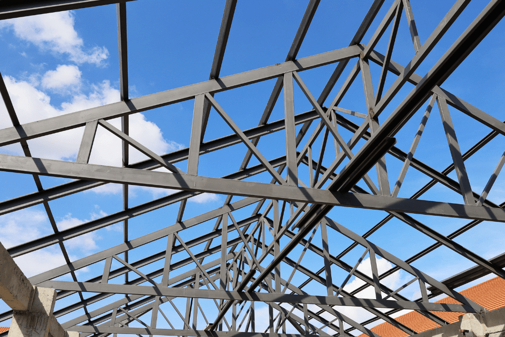 Metal trusses by ADCO Metals in LA & MS. Image shows exposed steel framing against a bright blue sky, highlighting structural support for a new metal building roof.