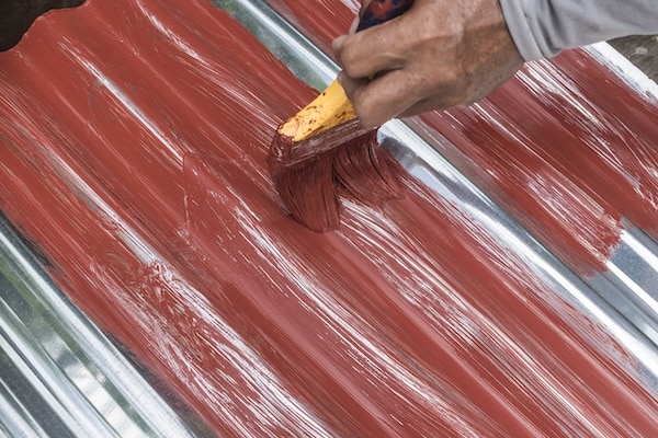 Painting the surface of a sheet of Galvanized Iron or GI corrugated metal with rust inhibiting red oxide primer to showcase how to repaint a metal roof.