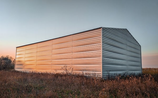 Warehouse constructed of corrugated galvanized iron. Warehouse in autumn during sunset in a field.