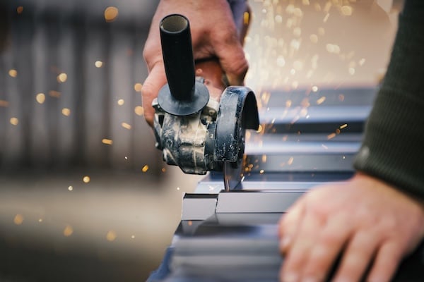 Building contractor is cutting lightweight metal, steel, corrugated, paint coated roofing sheet with an electric angle grinder