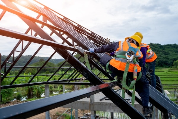 Construction worker wearing safety harness demonstrating an answer to the question are steel buildings cheaper than wood