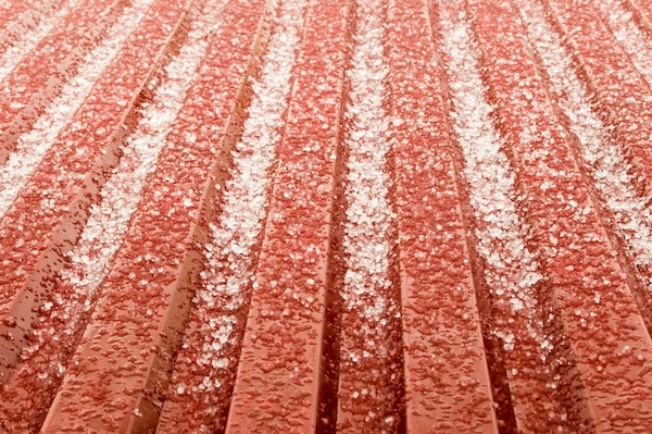 Hail accumulating on a red corrugated roof demonstrates an answer to the question can hail damage a metal roof