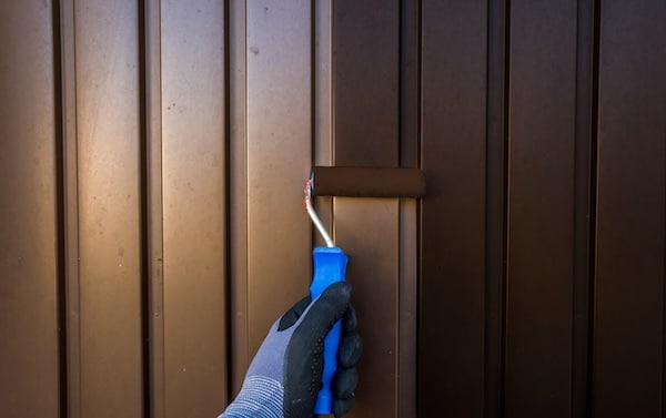 Worker hand paints sheet metal surface with paint roller answering the question can you paint a metal roof