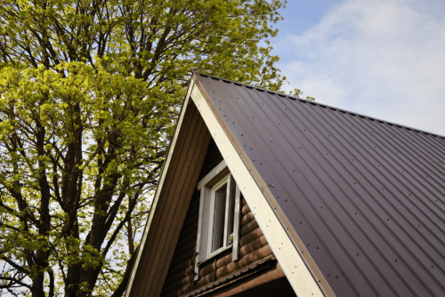 spring roof inspections, Metal Roofing In Lacombe, LA, At ADCO Metals. A-frame cabin with a brown metal roof surrounded by blooming trees